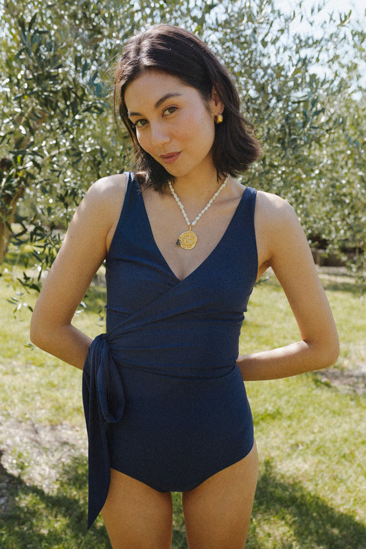 Woman wears a navy blue swimsuit with a bow tied at the hip.
