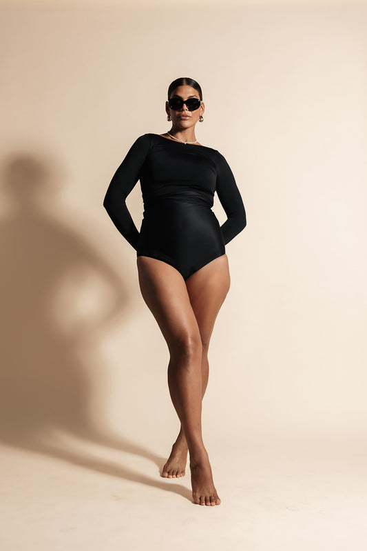 Woman wearing a black long sleeve wrap top with matching high waisted bikini bottoms. The combination creates the illusion of a long sleeve bodysuit.