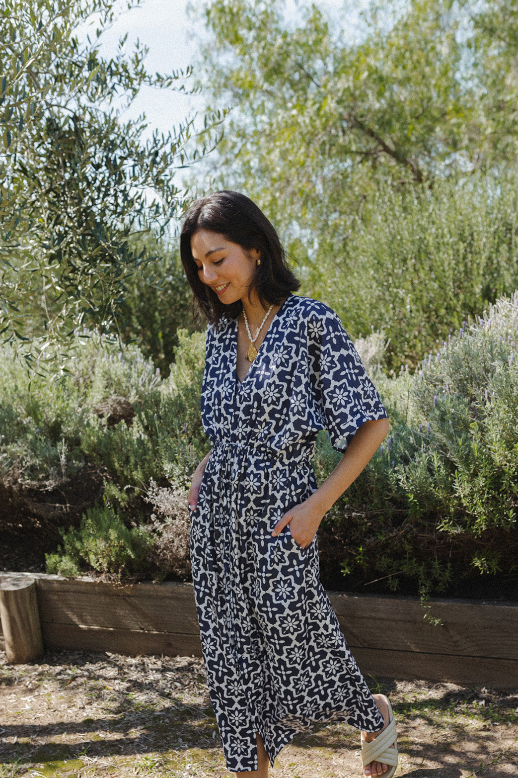 Woman walking through garden wearing navy blue maxi dress, with white geometric detailing.