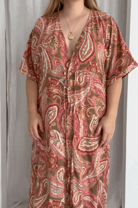 Woman adjusting the paisley pink print kaftan to her body shape by pulling the waist tie into a bow and locking in the clasp located on the bust area for modesty purposes