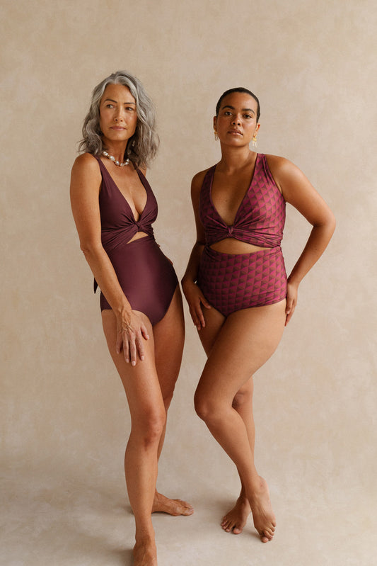 Two women wearing different reversible sides of the Monroe bikini set. The woman on the right wears the side featuring a striking burgundy geometric print, and the woman to her left wears the solid wine coloured side.