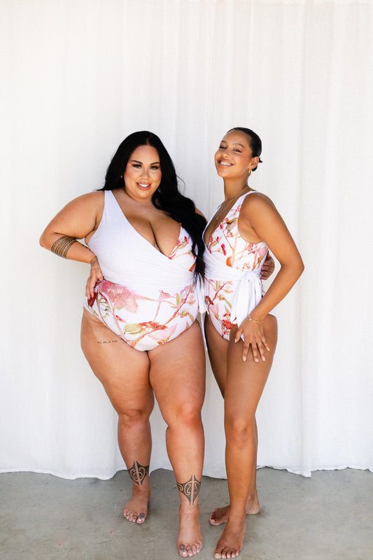 Two different sized women wearing matching white Banksia print one piece swimwear with waist ties.