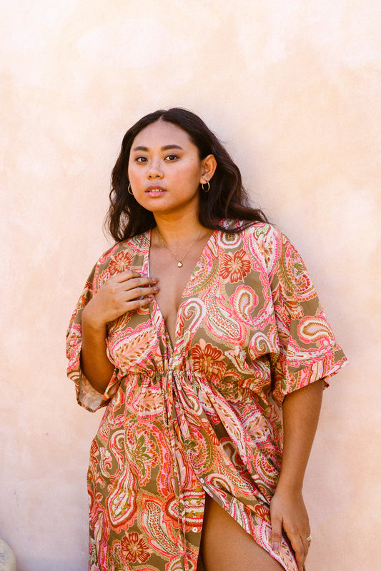Woman standing by beige stone wall dressed in the Barcelona kaftan which has been slightly left opened up by the bust and left thigh area for a sexier look