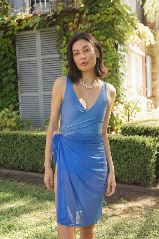 Woman wears reversible waterlily blue bikini top with a matching blue mesh sarong around her waist.