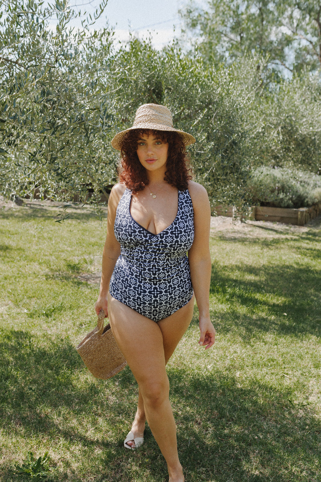 Woman walks through garden wearing a blue and white geometric bikini set.