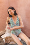 Woman is leaning against a ceramic statue, wearing a juniper green bikini with white tile pattern detailing.