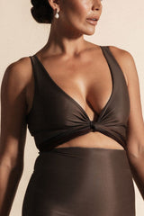 Woman stands in front of a beige background wearing a deep chocolate brown coloured bikini set. The top is cinched at the bust with a tie and the bottoms are high cut.