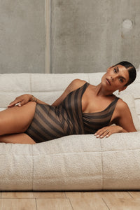 Woman in a relaxed pose lying on a white lounge, wearing a wrapsuit that features a diagonal striped print made up of decadent deep chocolate and light macchiato tones.