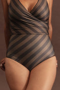 Woman leans on a stool wearing a deep chocolate and macchiato coloured bikini set with a bold diagonal stripe pattern.