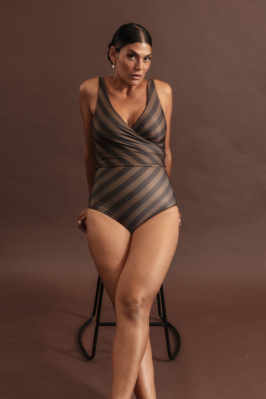 Woman leans on a stool wearing a deep chocolate and macchiato coloured bikini set with a bold diagonal stripe pattern.