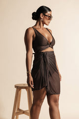 Woman poses next to a wooden stool wearing an espresso coloured bikini set with matching mesh sarong.