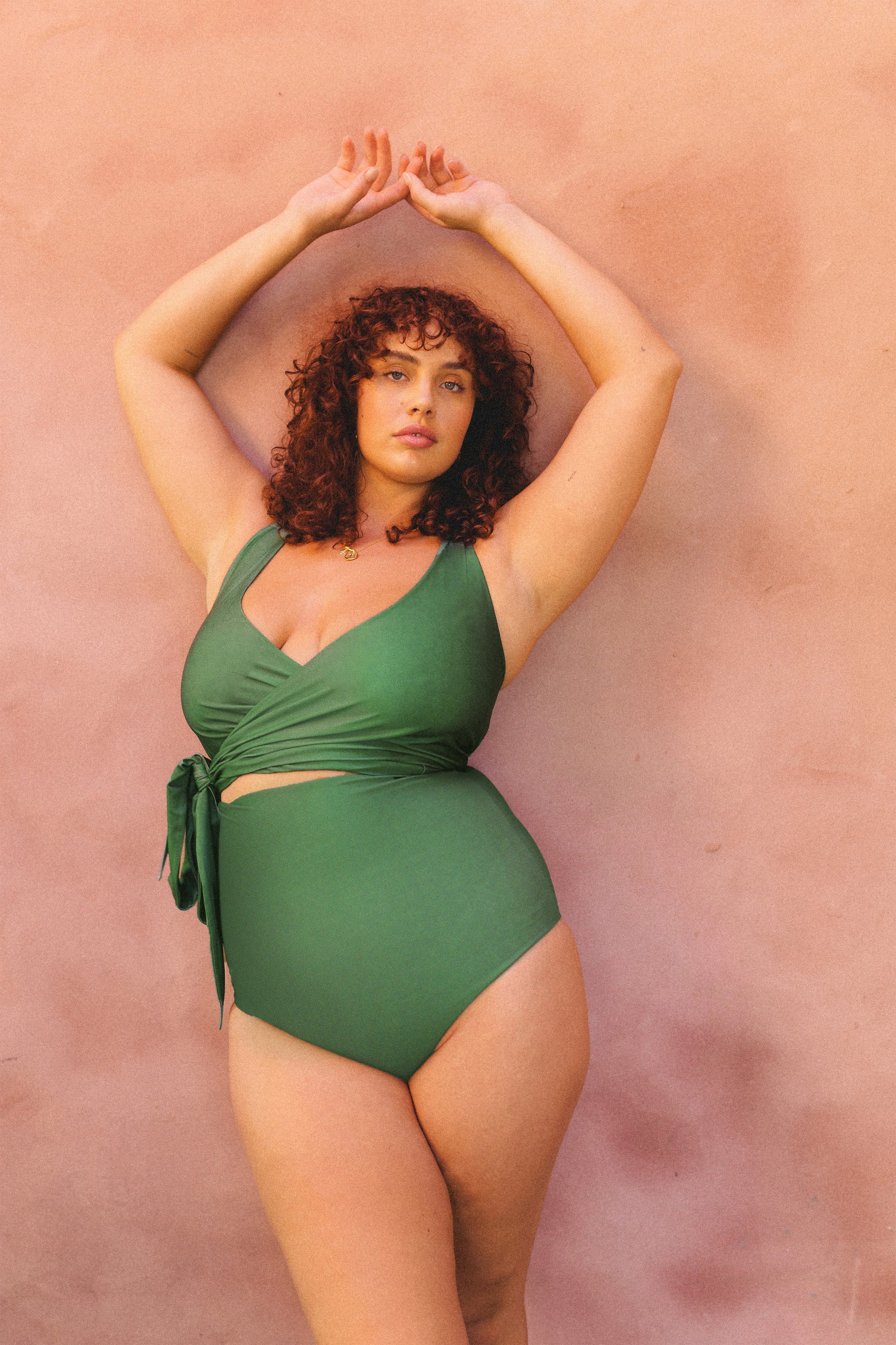 Woman leaning against wall, wearing a green 3 piece bikini.