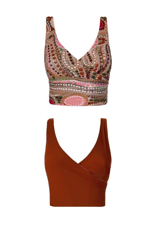 A woman stands at the waters edge in a hand painted bikini set. The indigenous print is comprised of vibrant pink, khaki and rust tones.
