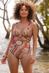 A woman stands at the waters edge in a hand painted bikini set. The indigenous print is comprised of vibrant pink, khaki and rust tones.