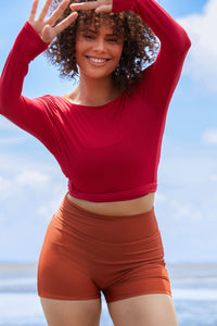 Woman wearing a raspberry coloured long sleeve wrap top with high waisted clay swim shorts.
