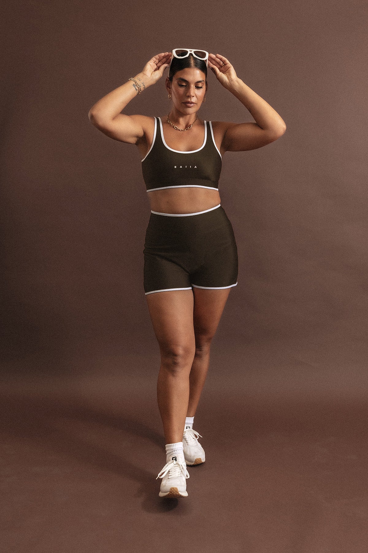 Woman wears a macchiato coloured swim set with white binding. The top is a scoop neck sports bra shape; and the bottoms are high waisted, sculpting shorts.