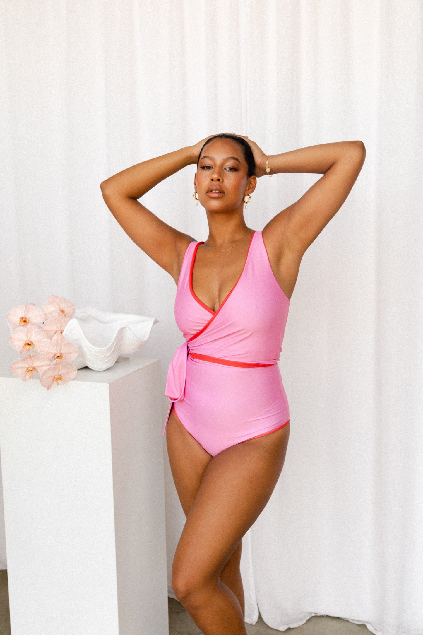 Woman wearing a playful pink bikini with red trim poses next to a plinth adorned with ocean ornaments.