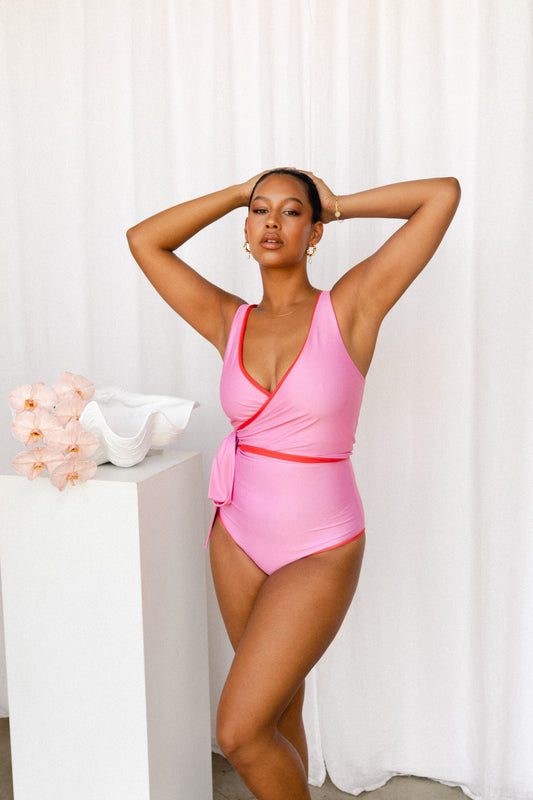 Woman wearing a playful pink bikini with red trim poses next to a plinth adorned with ocean ornaments.