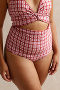 Woman wearing a deep, burnt coral pink coloured gingham print bikini set stands in front of a beige studio backdrop. 