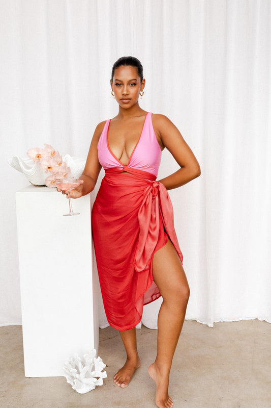 Woman wearing a pink bikini top with red trim matching the sarong tied at her waist.