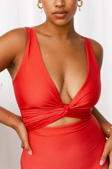 Woman wearing a coral red bikini set with tie cinching the bust to create a plunging neckline.