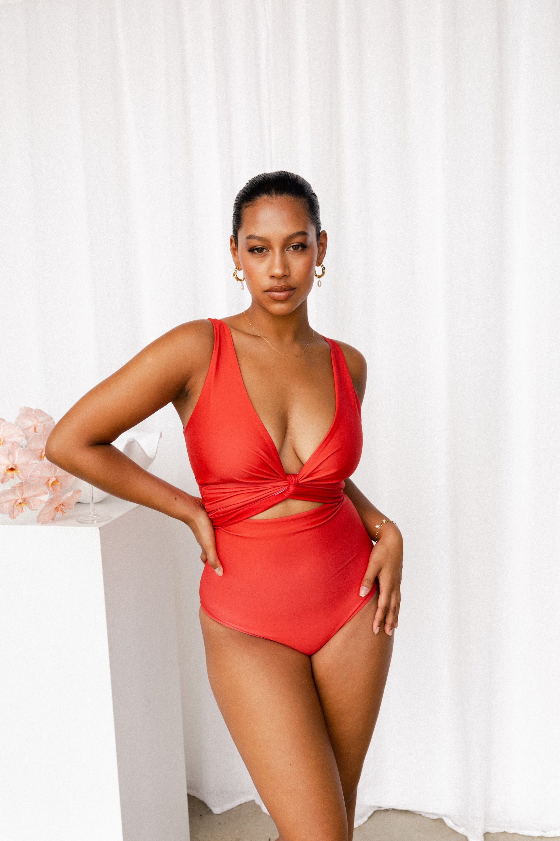 Woman wearing a coral red bikini set with tie cinching the bust to create a plunging neckline.