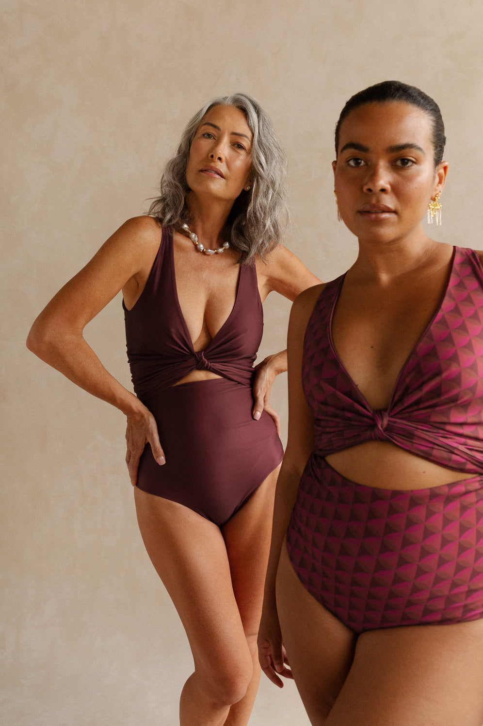 Two women wearing different reversible sides of the Monroe bikini set. The woman in the foreground wears the side featuring a striking burgundy geometric print, and the woman behind her wears the solid wine coloured side.