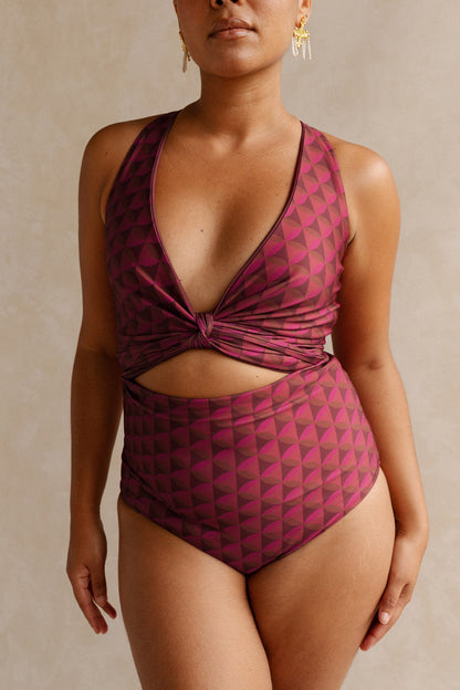 Woman wearing a burgundy toned bikini set featuring a geometric print. The top is cinched at the bust to provide a plunging neck line.