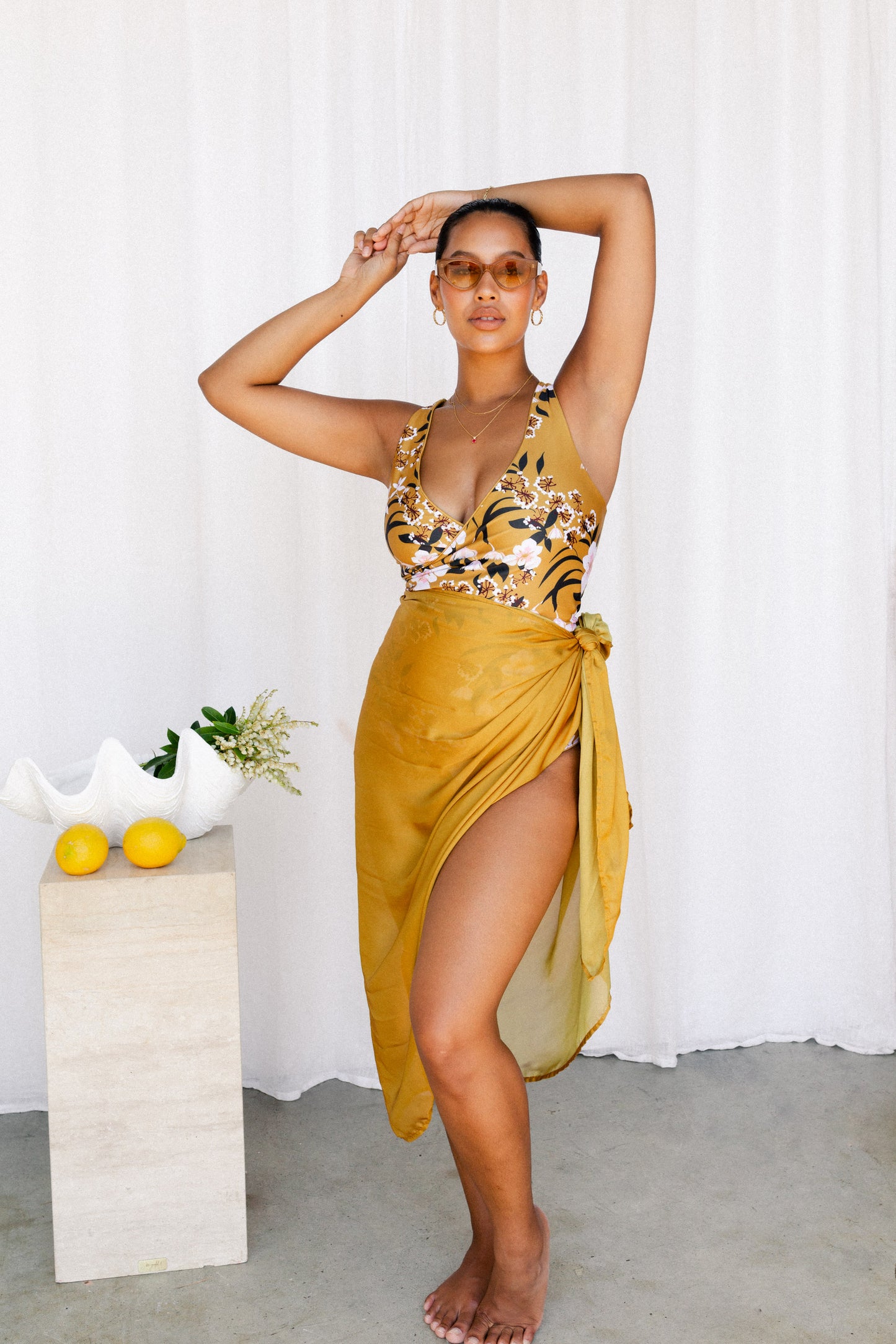 Woman poses in a mustard printed bikini set with matching sarong tied at the waist.