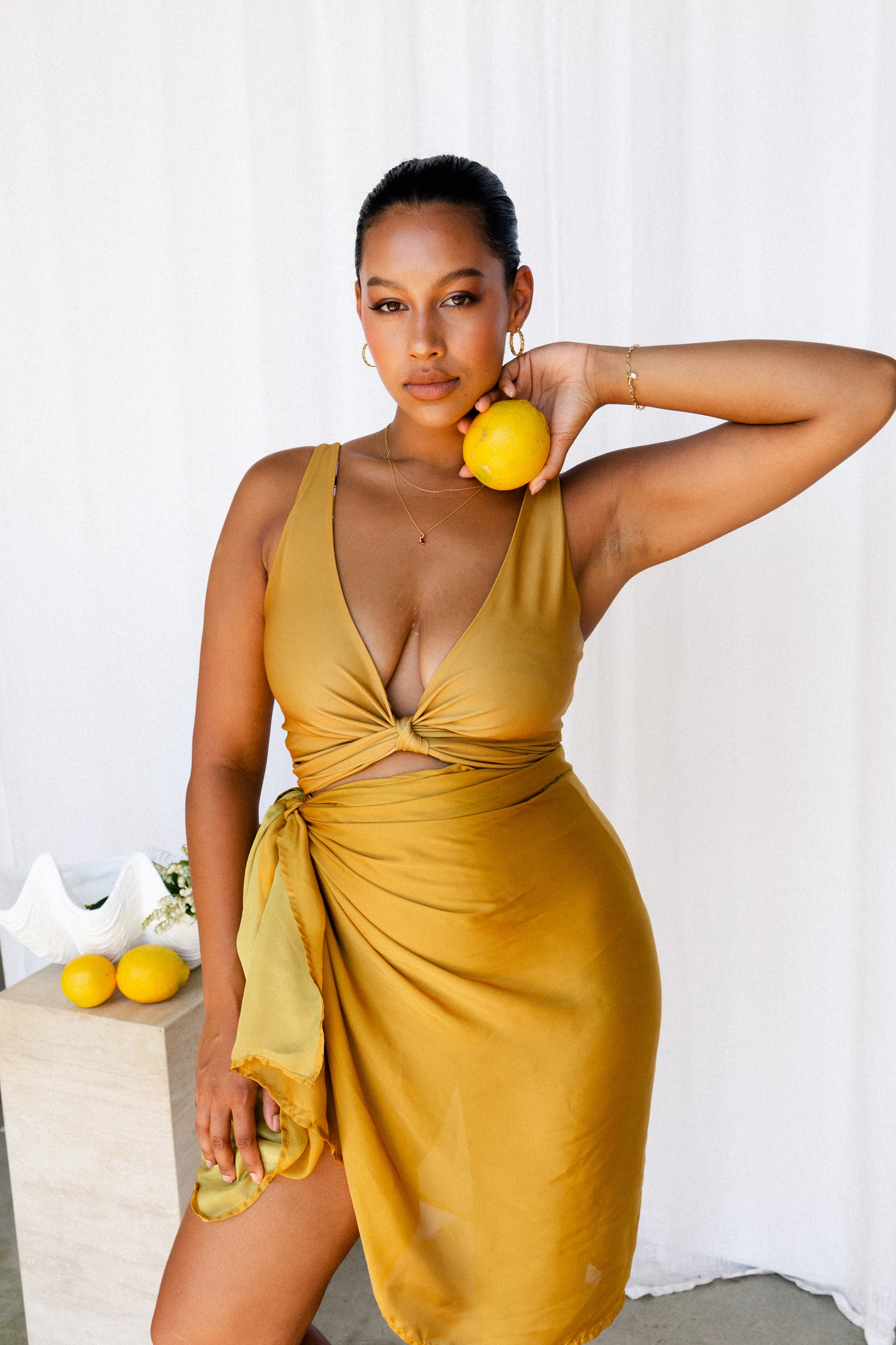 Woman holding a lemon wearing a matching mustard bikini set and sarong.