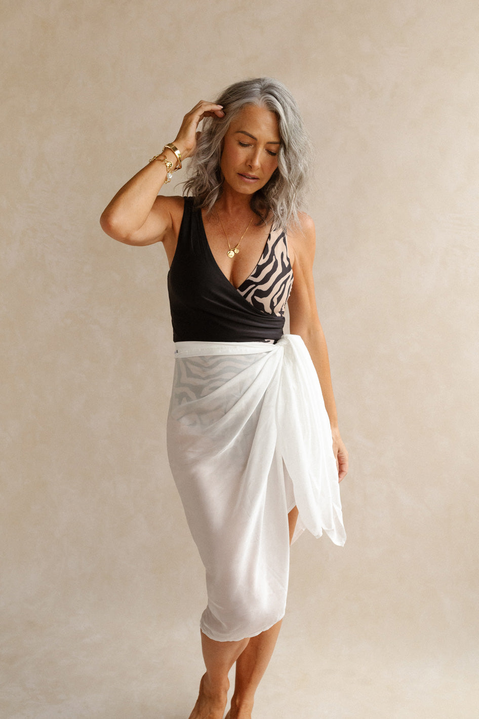 Woman wears a luxe white sarong around her waist, providing coverage for the swimsuit below.