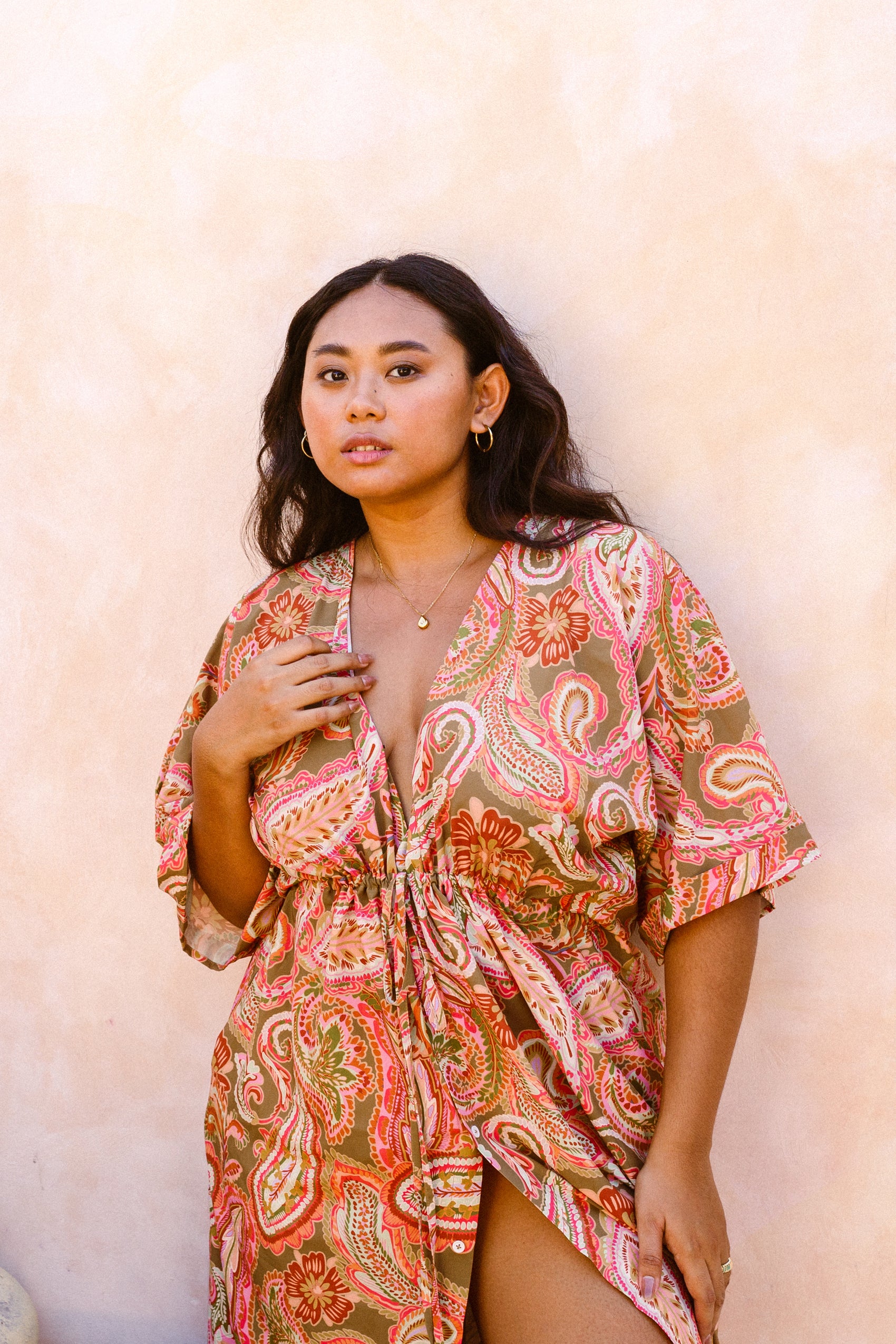 Woman standing by beige stone wall dressed in the Barcelona kaftan which has been slightly left opened up by the bust and left thigh area for a sexier look 