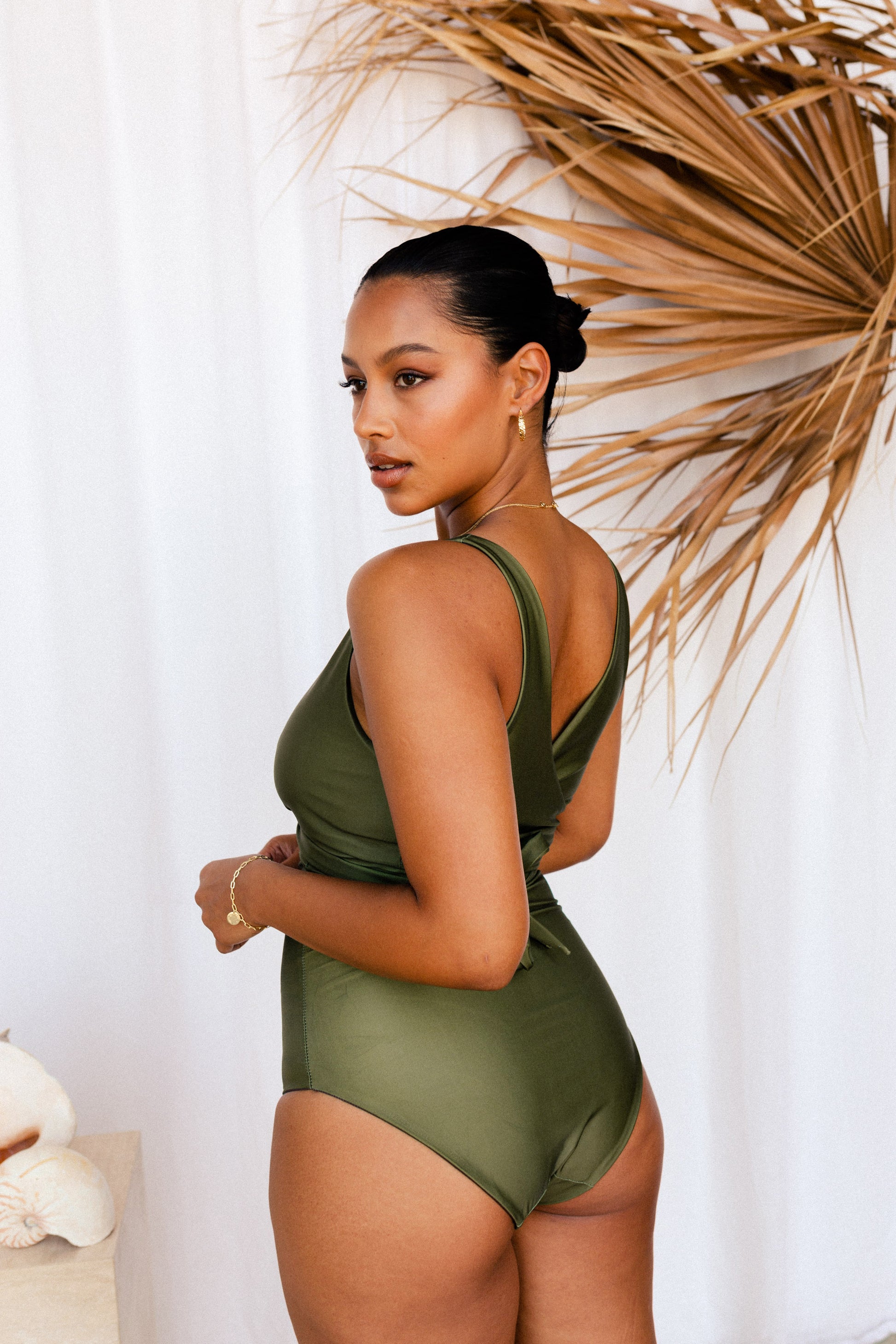 A woman poses in a khaki green bikini set, the photo is taken from behind to showcase the flattering bum coverage provided by the cut of the bottoms.