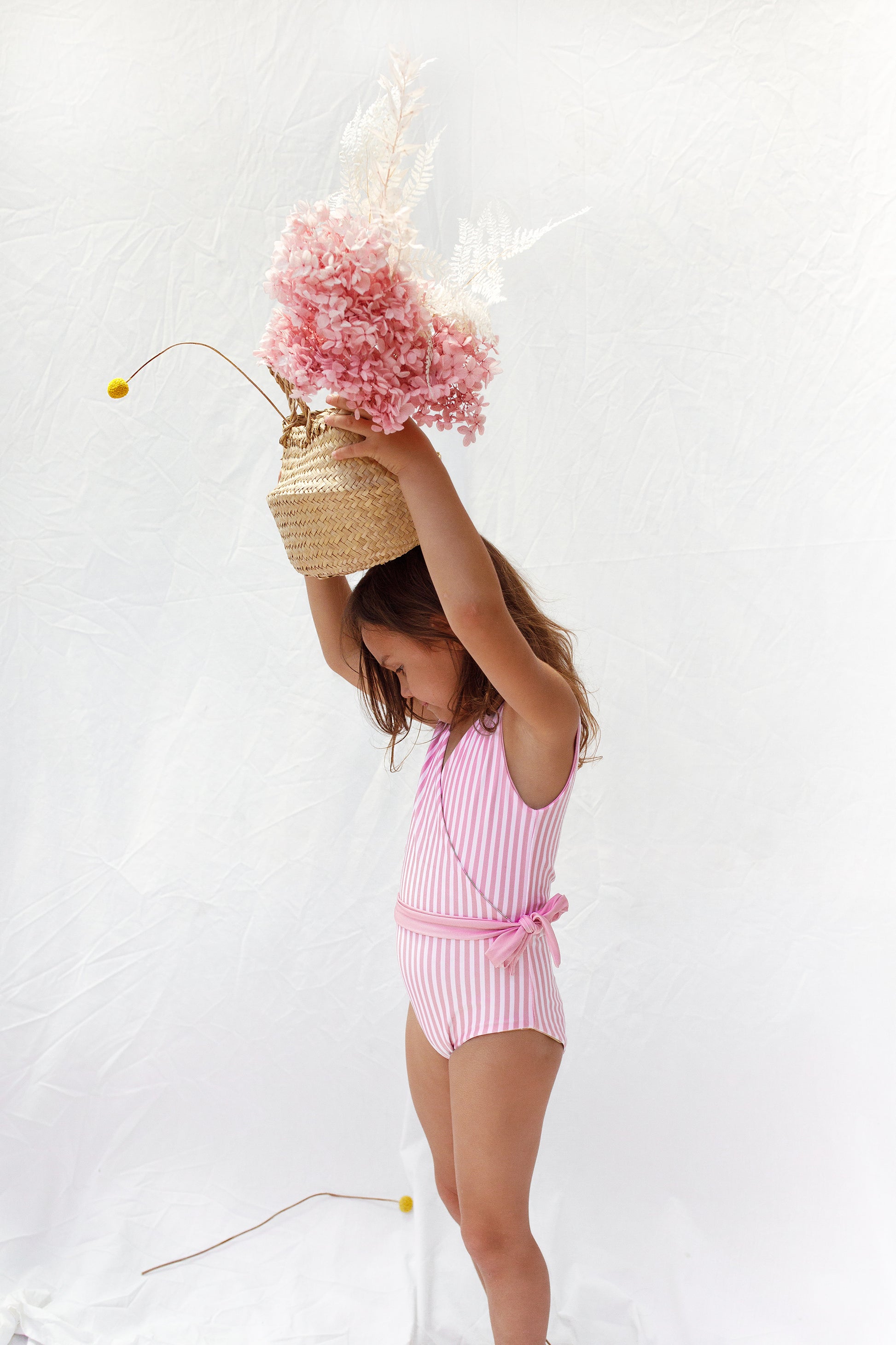 Side pose of girl in reversed pink and white stripe swimsuit with pink tie at waist
