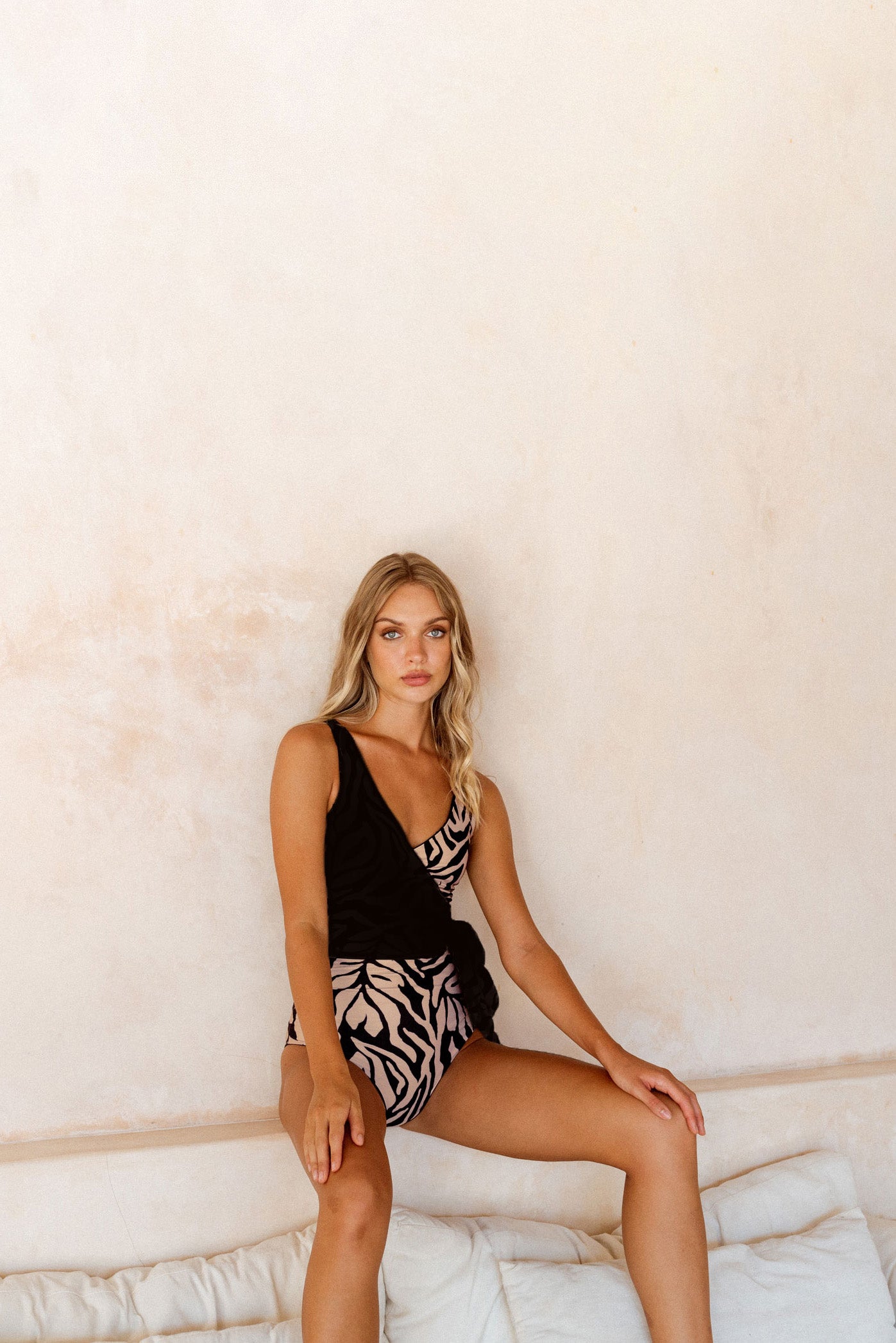 Woman sitting on stone corner wearing the luxurious Tulum wrapsuit with the body piece reversed to the animal print side